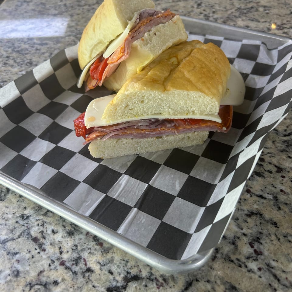 Deli sandwich with ham, cheese, tomato, and red onion served on a checkered paper-lined tray.
