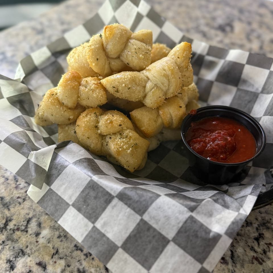 Golden garlic-seasoned bread bites served in a checkered basket with marinara dipping sauce.